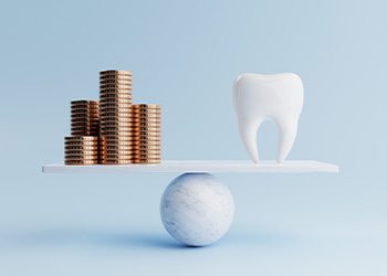 A dental tooth and golden coins on a balancing scale on blue background