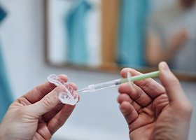 A dentist holding a teeth whitening tray and a gel-filled syringe